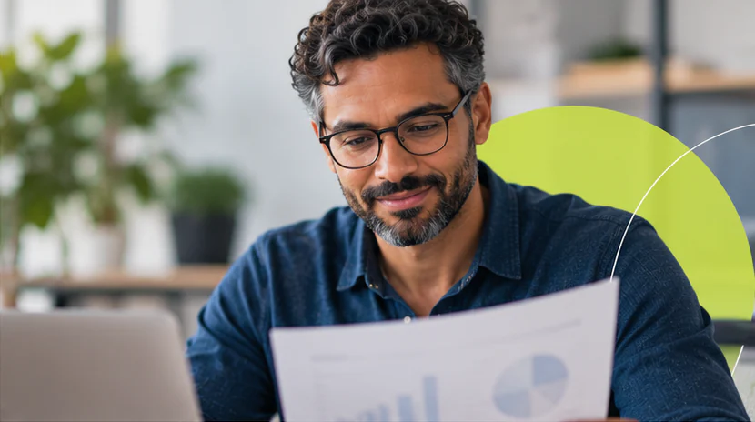 Homem de óculos lê, sorrindo, um relatório impresso com gráficos.