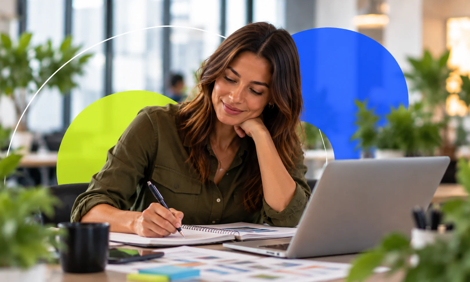 Mulher sorri enquanto faz anotações ao lado do notebook e de papéis com gráficos.